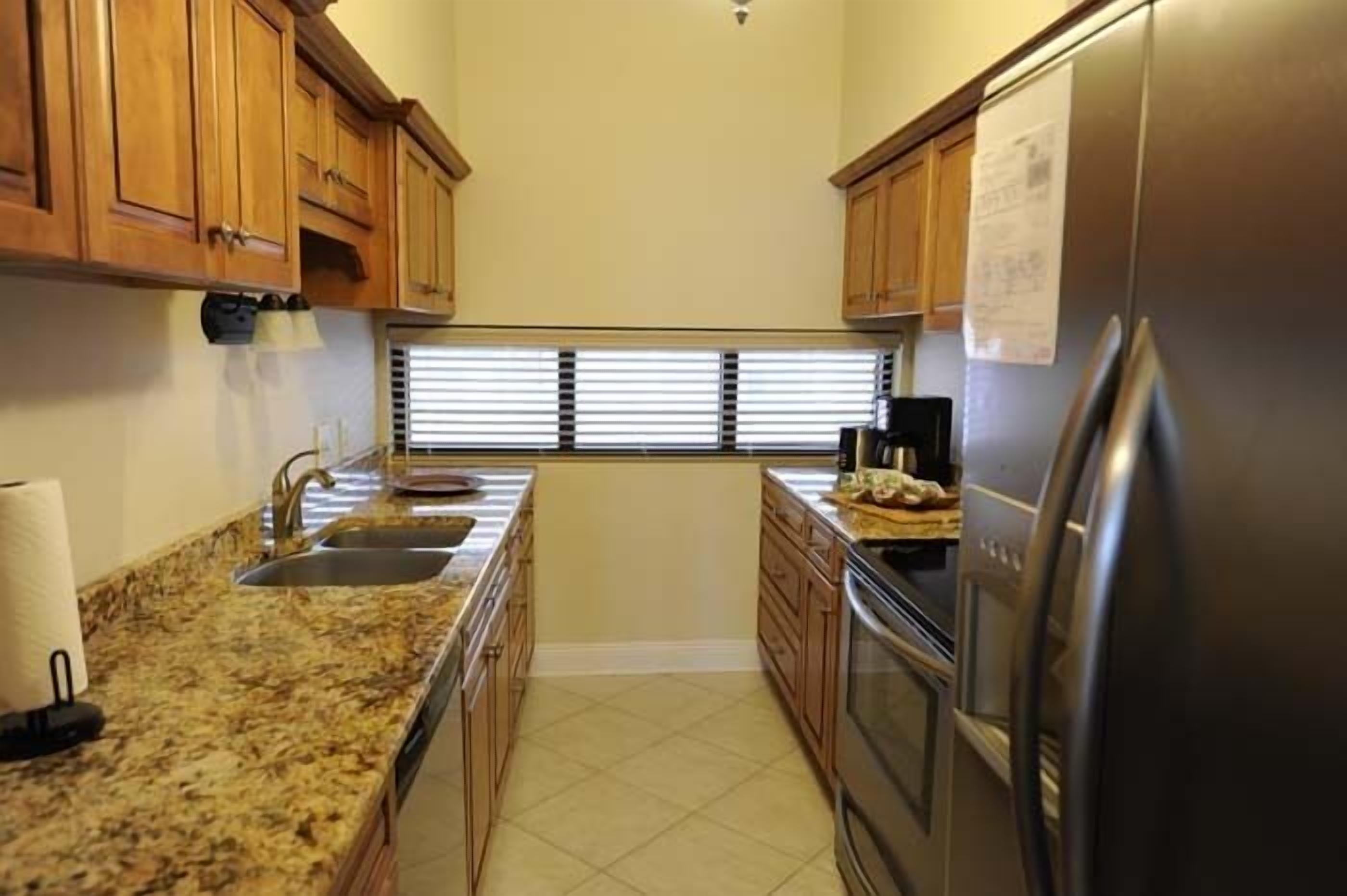 A kitchen with wooden cabinets, a stainless steel refrigerator, a sink, and a window with blinds.