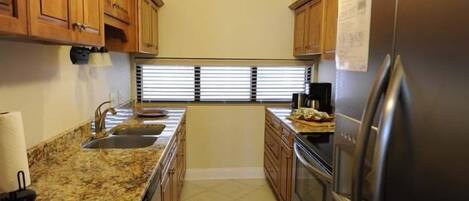 A kitchen with wooden cabinets, a stainless steel refrigerator, a sink, and a window with blinds.