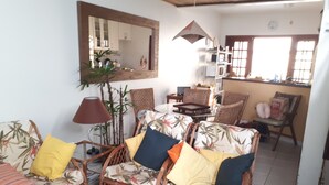 A living room with wicker furniture, a mirror, and a dining area with chairs and a table. - Charming house in a gated community in Juquehy. - 2 suites (São Sebastião)