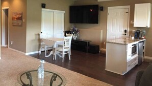 A compact living space with a dining area, kitchen, and a flat-screen TV mounted on the wall. - Lakeside Living Suite! ~Mt. Rainier, NWTrek, JBLM (Graham)