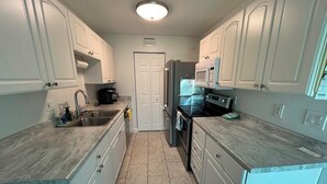 A compact kitchen with white cabinets, a sink, a stove, and a microwave.