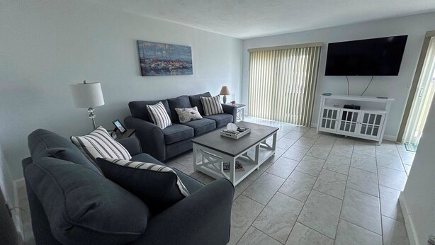 A modern living room with a dark grey sofa set, a coffee table, a flat-screen TV mounted on the wall, and a white cabinet with glass doors.
