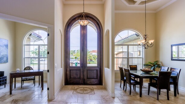 A spacious entryway with a large wooden door, a dining area with a glass table, and a view of the outdoors through large windows. - House Aruba by Vacationhit (Cape Coral)