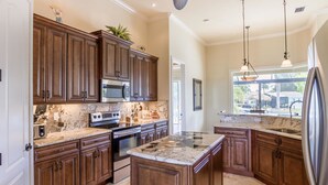 A modern kitchen with dark wood cabinets, granite countertops, stainless steel appliances, and a large island. - House Aruba by Vacationhit (Cape Coral)