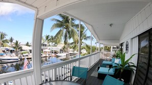 Un espace extérieur abrité, doté d’une table et de chaises, qui offre une vue sur une marina avec des bateaux et des palmiers.