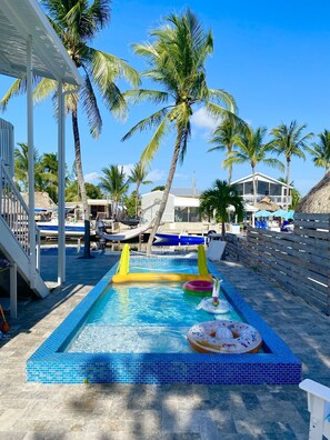 Une piscine dont le bord est recouvert de carreaux bleus, entourée de palmiers et dotée d’une terrasse en bois.