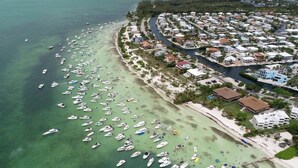 Une vue aérienne d’une zone côtière où de nombreux bateaux sont amarrés le long de la rive, ainsi qu’une zone résidentielle avec des bâtiments et des routes.