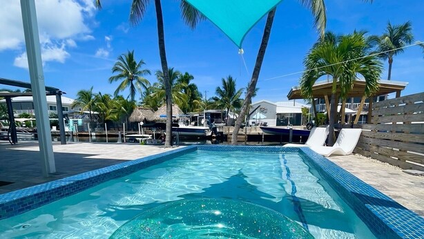Une piscine d’un bleu éclatant, avec un flotteur circulaire portant l’inscription « MMO », et un auvent bleu au-dessus.