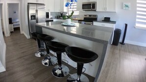 Une cuisine moderne avec des meubles blancs, des appareils en acier inoxydable et un îlot central doté de tabourets de bar.