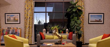 A modern lobby with a sofa, two yellow armchairs, a wooden coffee table, and a large potted plant.