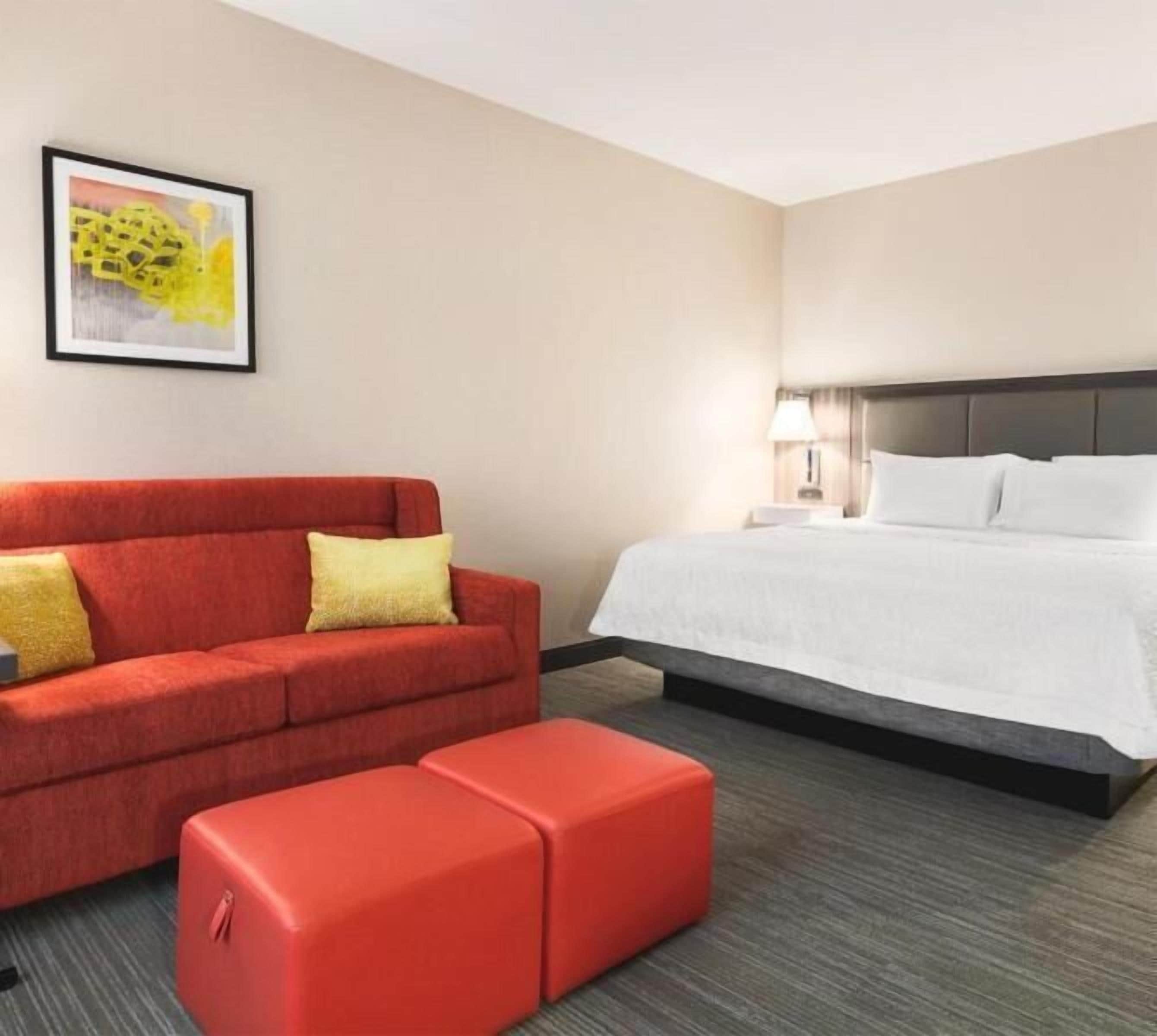 A hotel room with a red sofa, a white bed, and a small red ottoman.