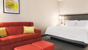 A hotel room with a red sofa, a white bed, and a small red ottoman.
