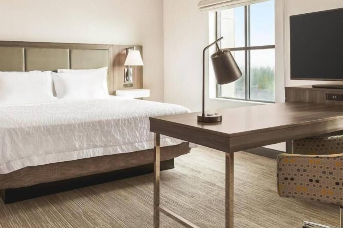 A hotel room with a bed, a desk, a lamp, a TV, and a window.