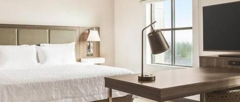 A hotel room with a bed, a desk, a lamp, a TV, and a window.
