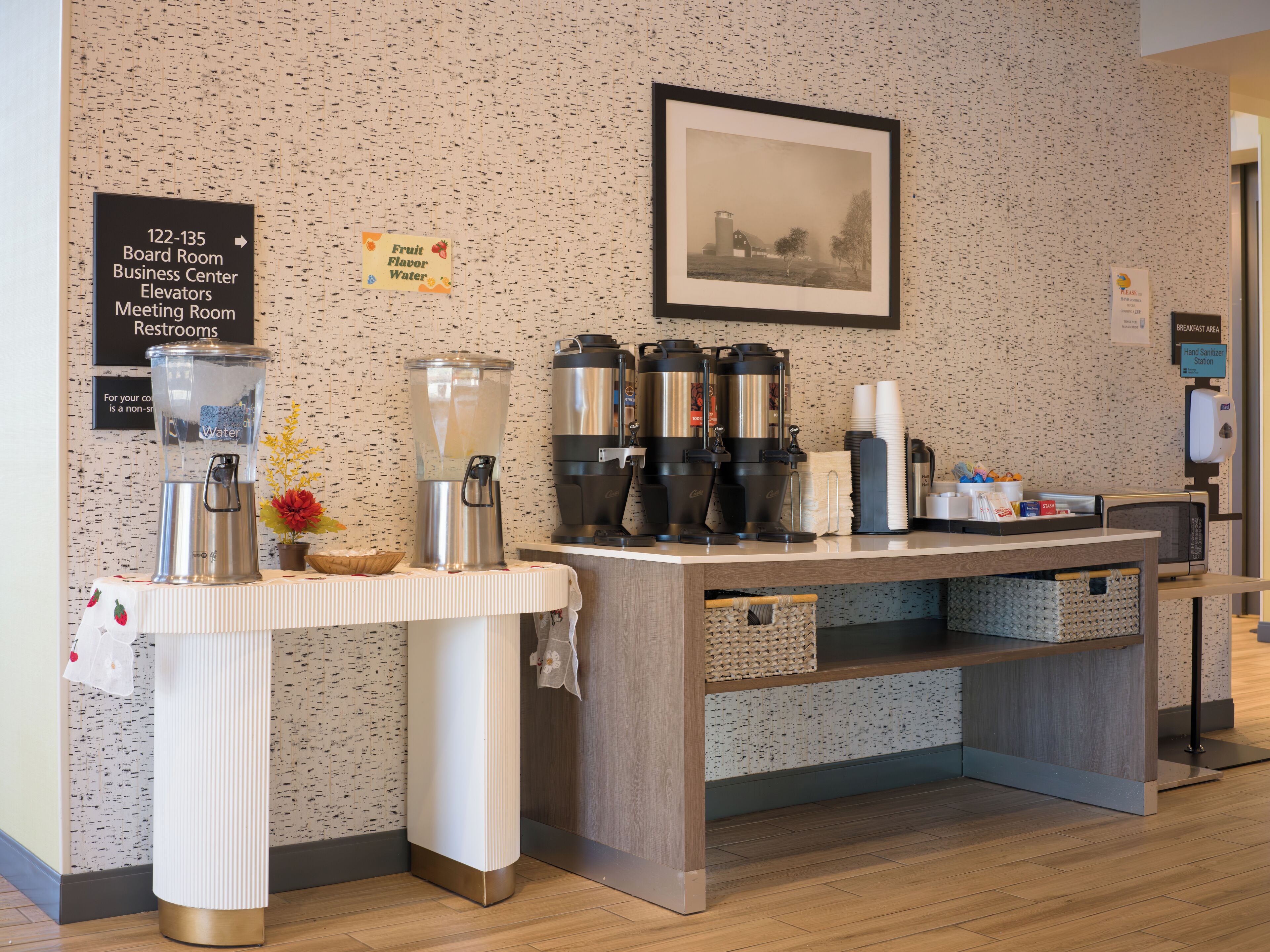 Un espace dédié au café, équipé d’un distributeur d’eau, de machines à café et d’un panneau indiquant l’emplacement de la salle de réunion, du centre d’affaires, des ascenseurs, de la salle de conférence et des toilettes.