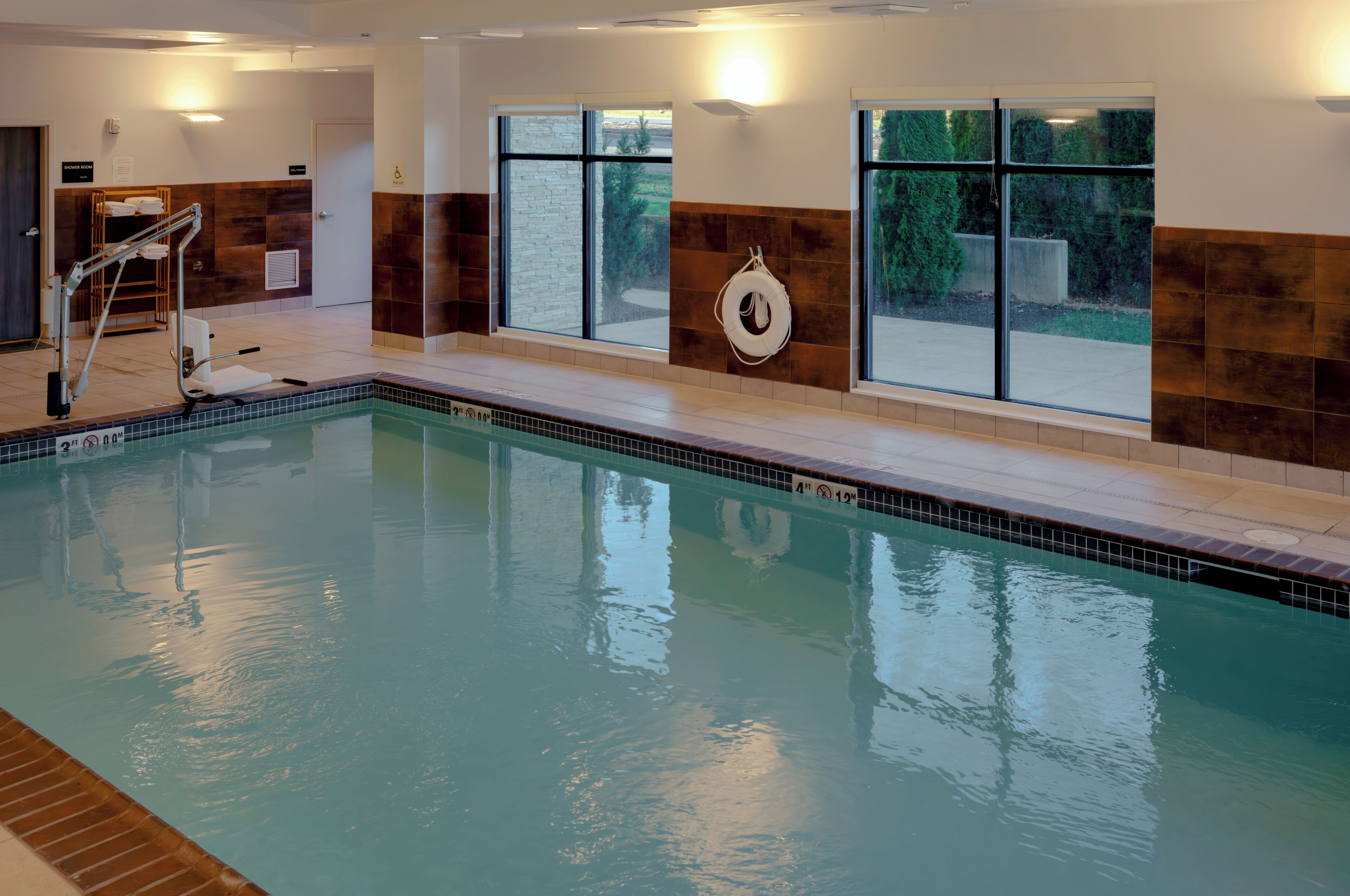 An indoor swimming pool with clear water, a lifeguard chair, and a towel rack.