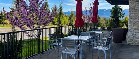 An outdoor patio with tables and chairs, surrounded by a stone wall and a metal fence.