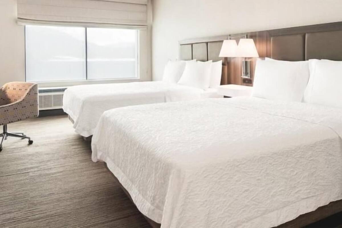 A hotel room with two beds, a desk, and a chair.