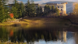 A lakeside view with a modern building, trees, and a stone bridge. - Snoqualmie Inn by Hotel America (Snoqualmie)