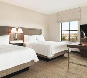 A hotel room with two beds, a desk, a lamp, and a large window with a view.