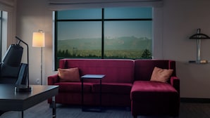 A room with a red sofa, a small table, a lamp, and a view of mountains through large windows. - Snoqualmie Inn by Hotel America (Snoqualmie)