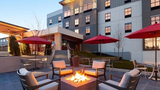 An outdoor patio area with a fire pit surrounded by chairs and red umbrellas, overlooking a building with multiple windows and a staircase. - Snoqualmie Inn by Hotel America (Snoqualmie)