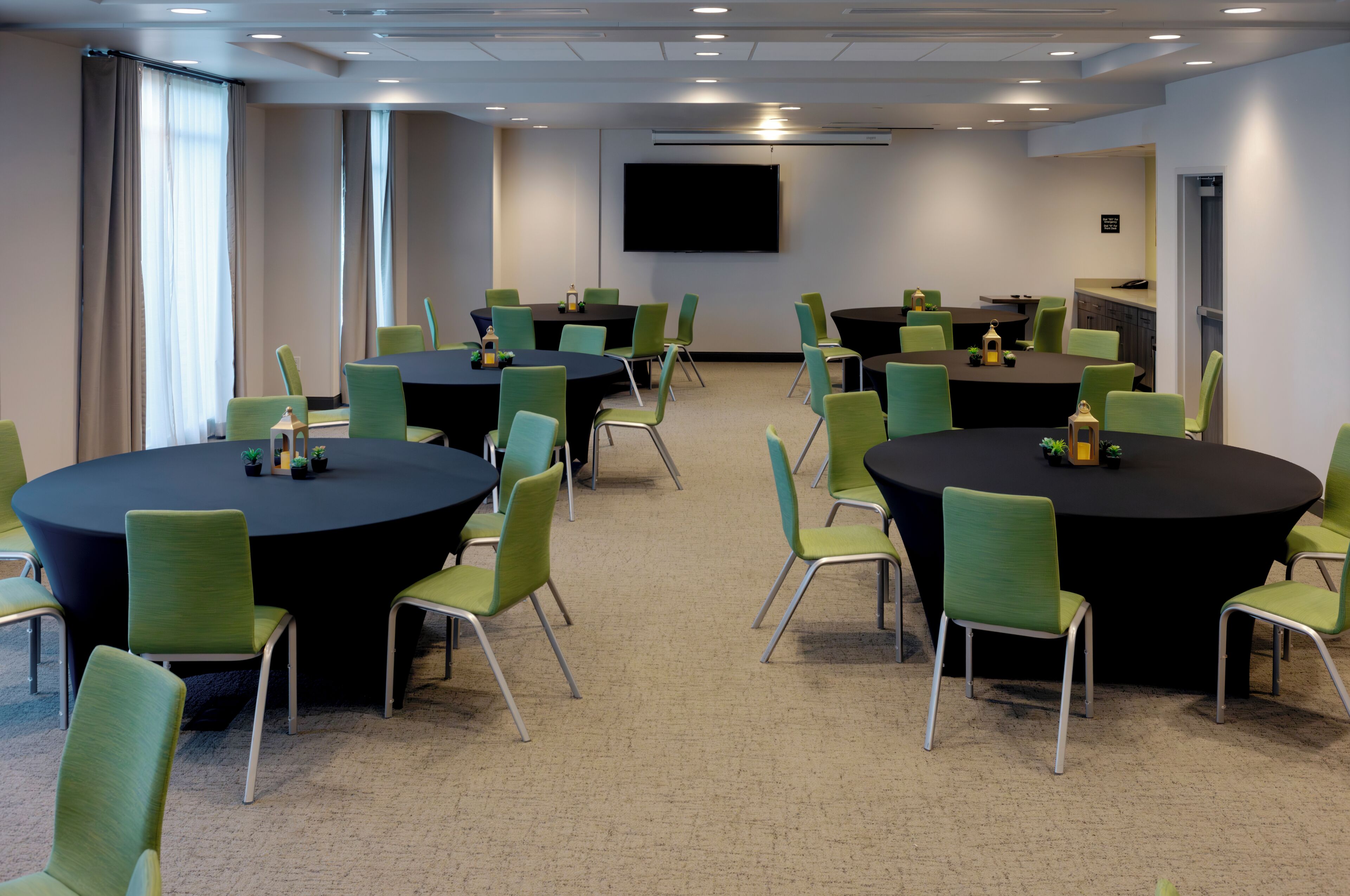 A conference room with multiple round tables and green chairs, equipped with small potted plants and candles.