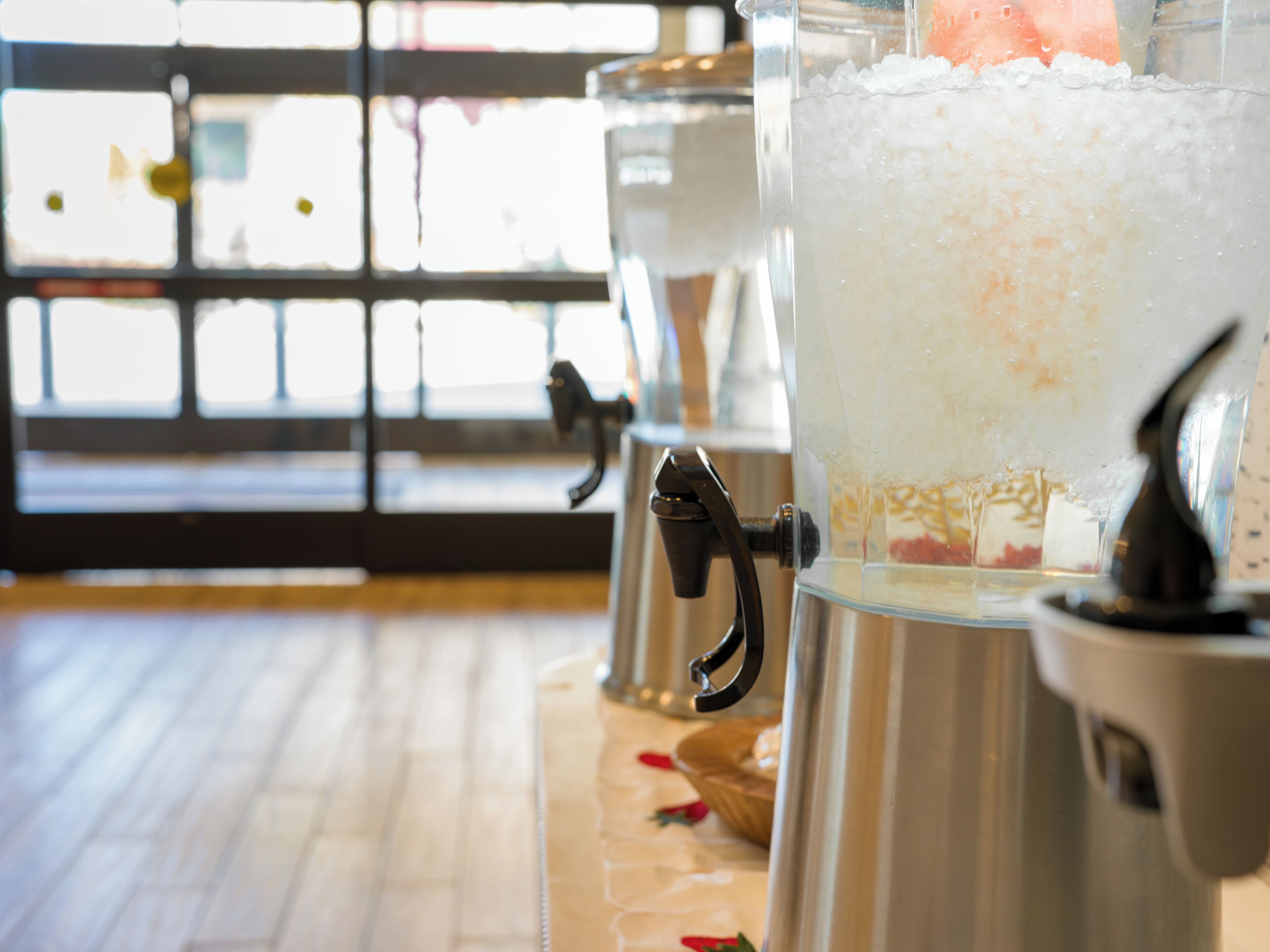 A row of beverage dispensers with a frosty beverage, a metal handle, and a glass container.