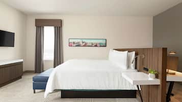 A modern hotel room with a large bed, a bedside table with a lamp, a flat-screen TV mounted on the wall, a cityscape painting, and a window with curtains.