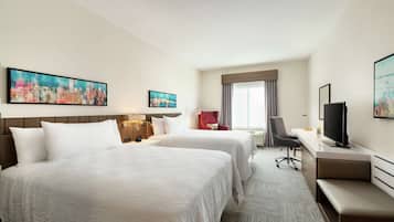A hotel room with two beds, a desk, a TV, and artwork on the walls.
