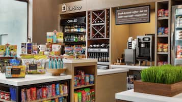 A coffee shop interior with shelves stocked with snacks, a coffee machine, and a display of bottled beverages.