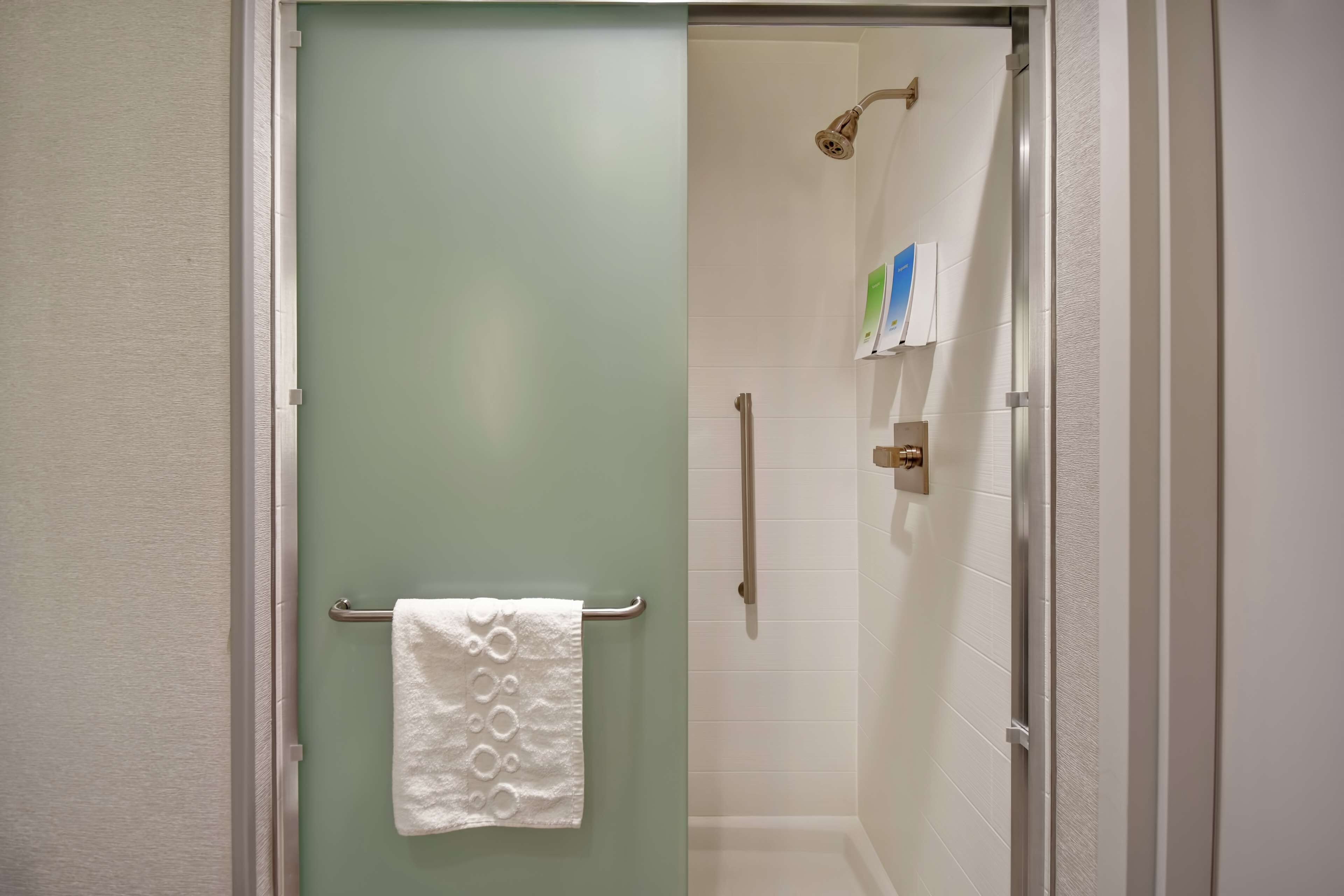 A bathroom with a shower, a towel rack with a white towel, and a glass shower door.