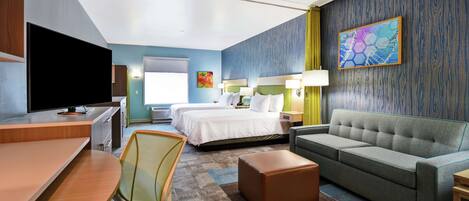 Quarto de hotel com cama, sofá, escrivaninha, televisão e um quadro na parede.