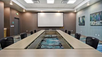 Une salle de conférence avec une longue table, des chaises, un écran de projection et un sol recouvert de moquette.