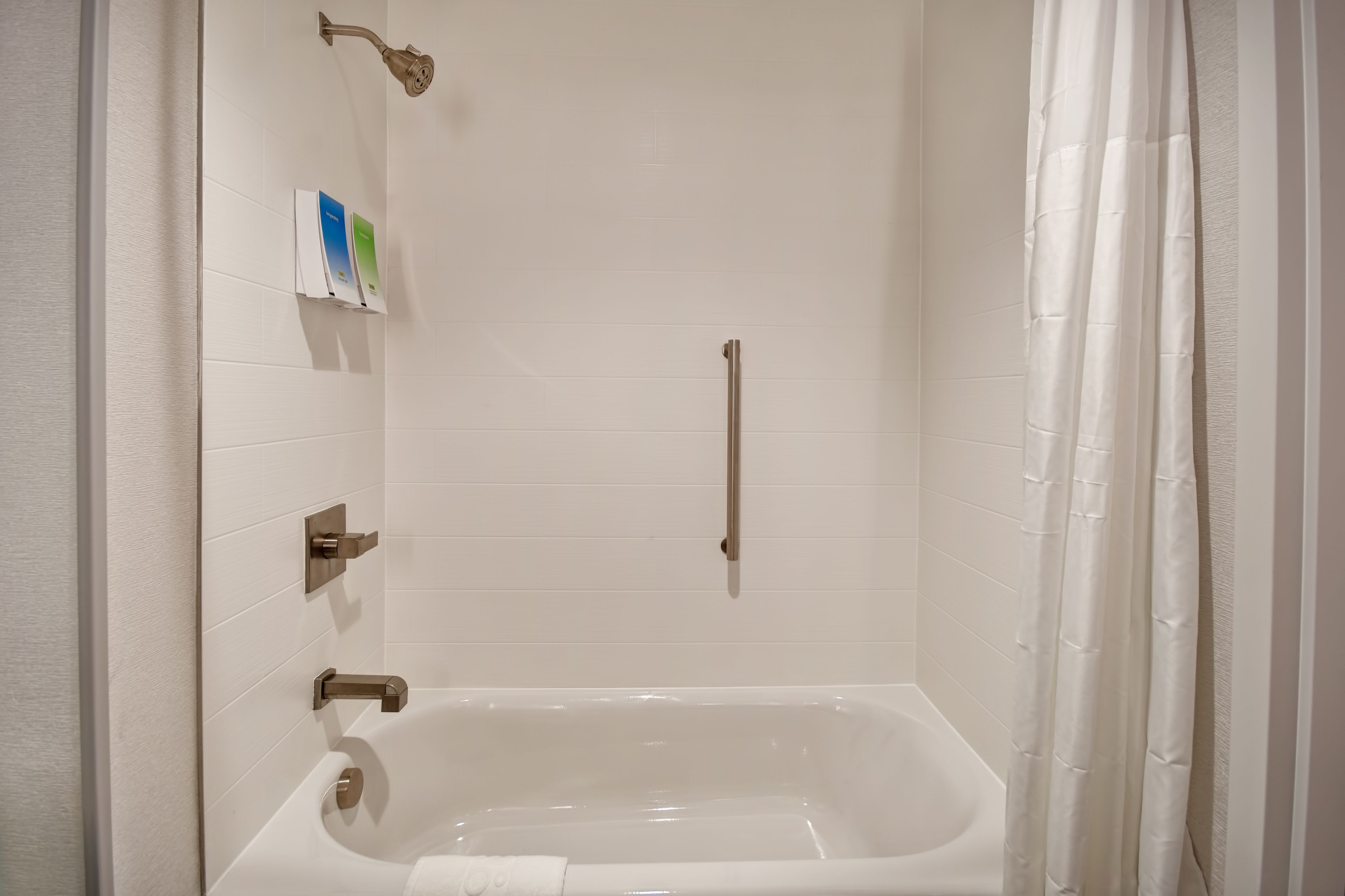 A modern bathroom with a bathtub, a showerhead, and a handrail.