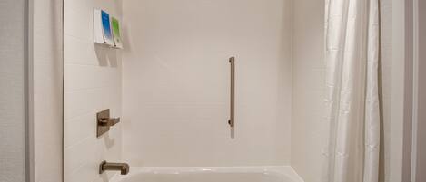 A modern bathroom with a bathtub, a showerhead, and a handrail.