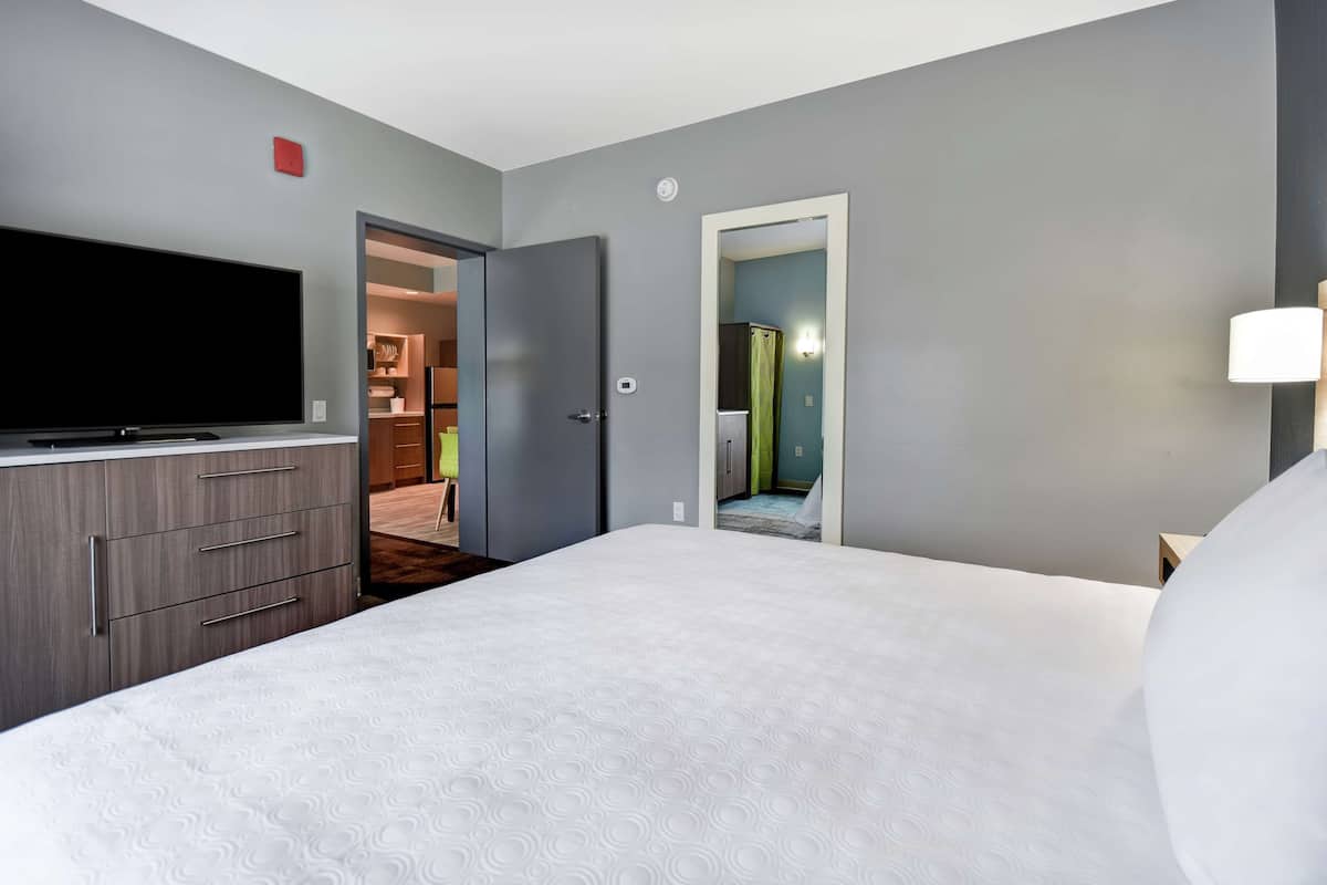 Habitación de hotel con una cama grande, un televisor de pantalla plana, un aparador y una puerta que da a un baño.