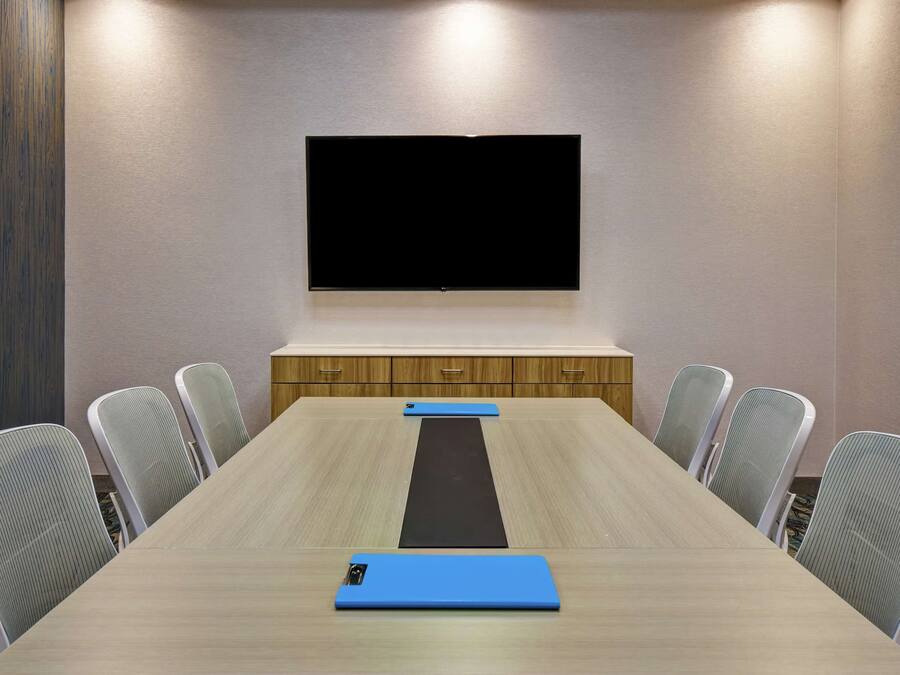 Ein Konferenzraum mit einem langen Tisch, sechs Stühlen, einer schwarzen Matte und einer blauen Matte auf dem Boden.