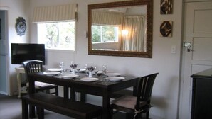 Un comedor con una mesa de madera oscura dispuesta para cuatro personas, un televisor sobre una mesita a la izquierda y un espejo grande sobre la mesa.
