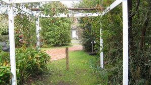 Un sendero en un jardín que lleva a una estructura de pérgola blanca, rodeada de exuberante follaje y plantas.