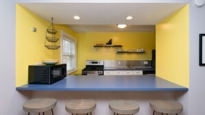 Een keuken met een blauw aanrecht, vier krukken, een magnetron, een fornuis en een hangende lamp.