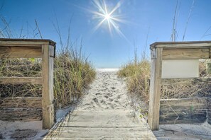 Ein hölzerner Weg führt zu einem Strand, der von einem klaren Himmel und Sonnenschein erhellt wird.