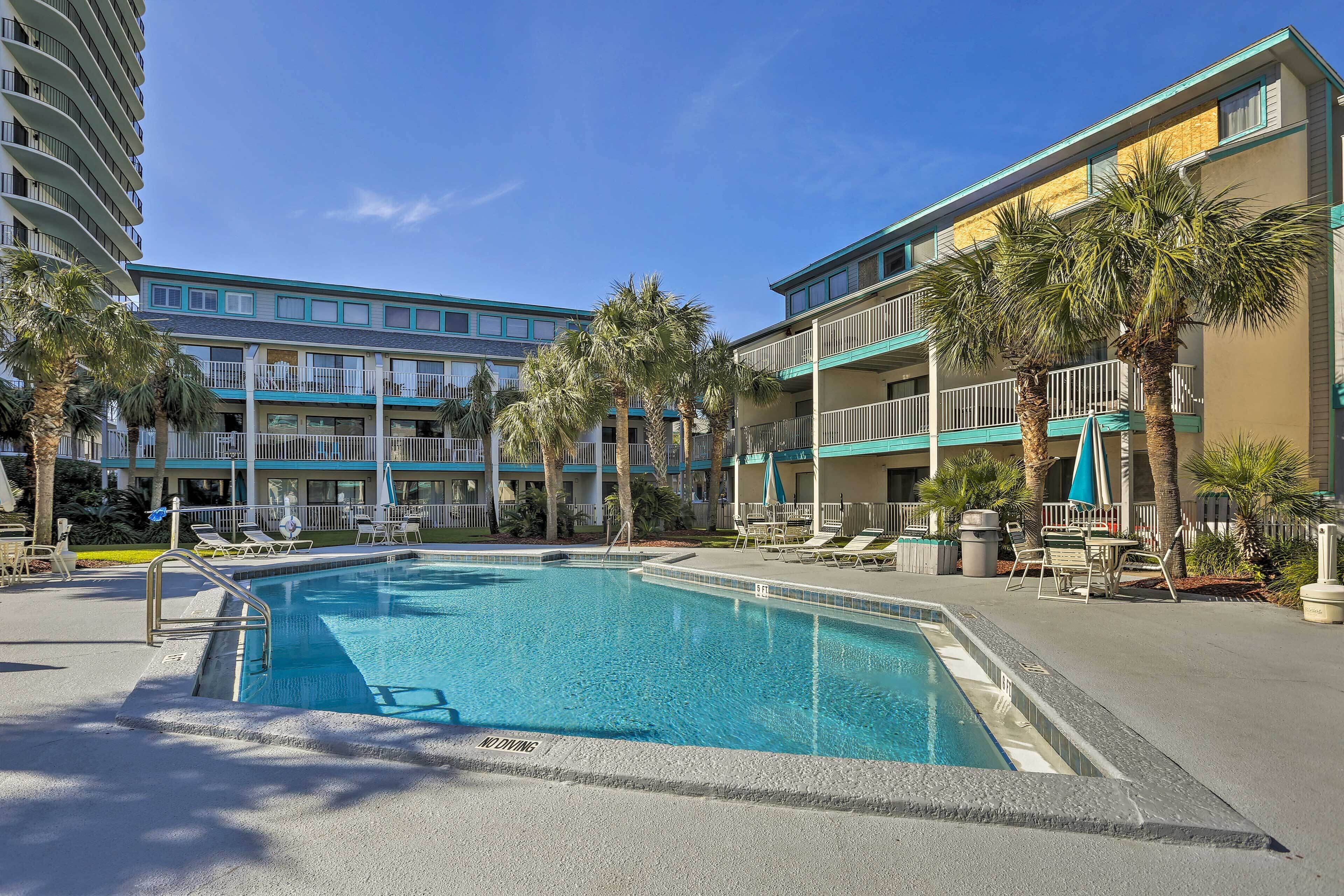 Ein Hotelpoolbereich mit klarem, blauem Wasser, Liegestühlen und Palmen.