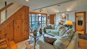 A spacious living room with a staircase, a large window offering a view of the outdoors, and a comfortable seating area with a sofa and a coffee table. - Lake Champlain Cottage w/ Private Deck & Fire Pit! (North Hero)