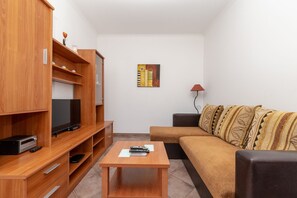 Uma sala de estar moderna com um rack de madeira, uma TV de tela plana, um sofá com almofadas estampadas e uma mesinha com controles remotos.