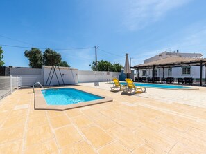 Área da piscina com duas piscinas, espreguiçadeiras e um espaço coberto para relaxar.