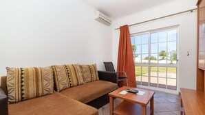 Een moderne woonkamer met een bruine bank, een houten tafel en een groot raam met uitzicht op het omliggende landschap.