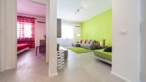 Un salon moderne avec un mur d’accent vert, un canapé gris et un lit rouge.