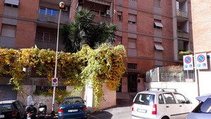 Un immeuble résidentiel à plusieurs étages, doté de balcons, d’un espace de stationnement et d’un arbre aux feuilles jaunes.