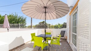 An outdoor patio with a table and chairs, a large umbrella, and a white fence in the background.